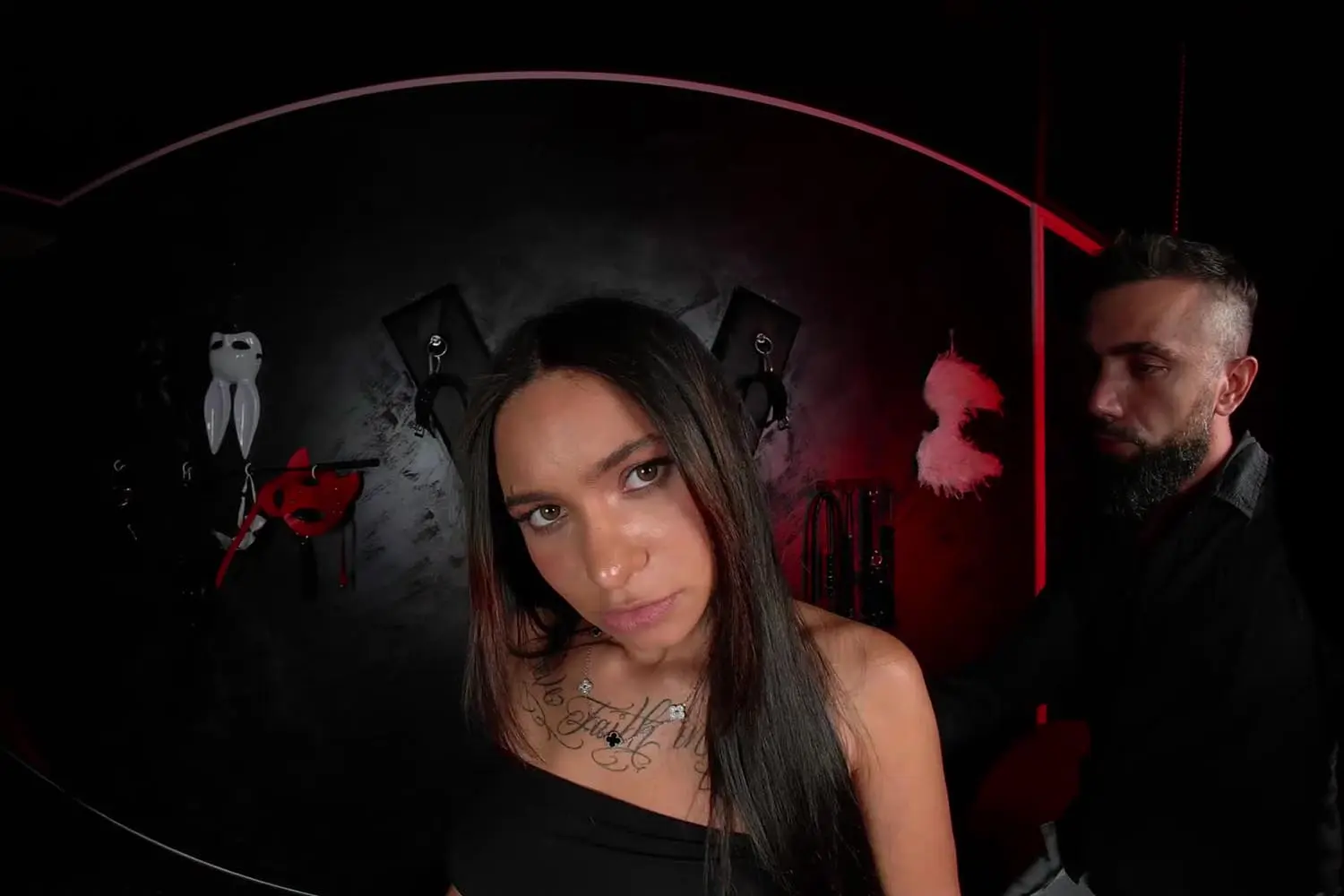 Agatha Santos in a red-lit BDSM room with a stranger behind her, the cuckold VR porn scene Rough on a Perky Butt on VRPorn.com